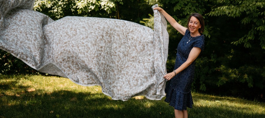 Kristen Detton standing outside holding a length of printed fabric as it blows in the breeze.