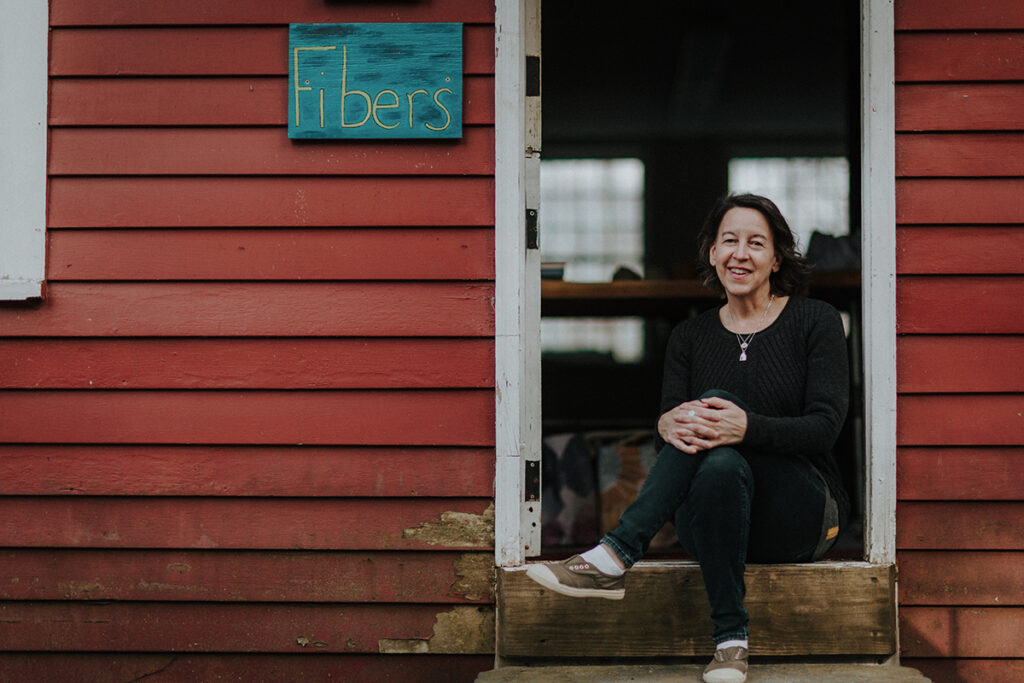 Kristen Dettoni sitting in front of the fiber studio at Snow Farm craft school.