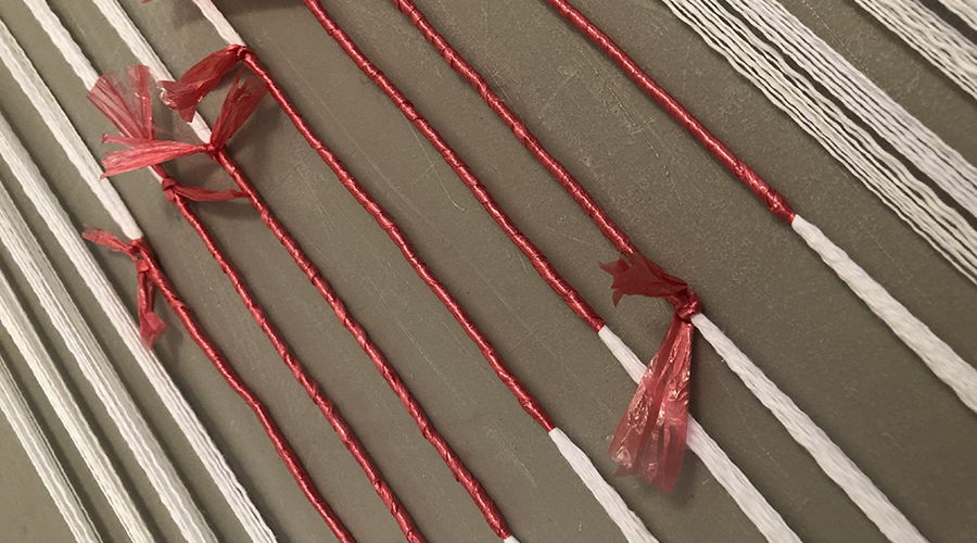 Warp threads bound with red plastic, showing how ikat threads are bound for dyeing.