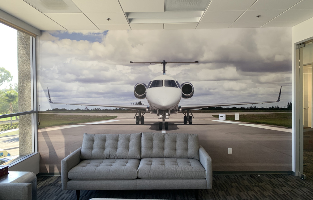 Photo of waiting room with couch and a wall graphic printed by Lucent Graphic Solutions showing a giant airplane.