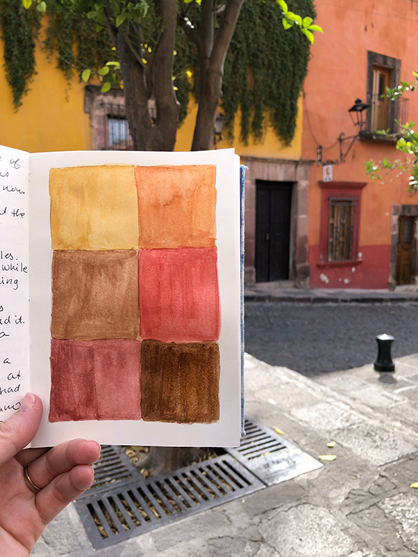 A photo of a travel journal held up to a street in San Miguel de Allende with color swatches, by Kristin Crane.